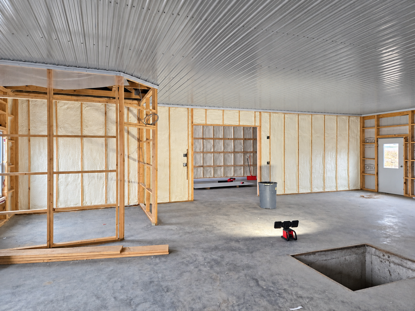 Workshop interior with spray foam insulation in the wall framing, exposed wood framing, and a corrugated metal ceiling