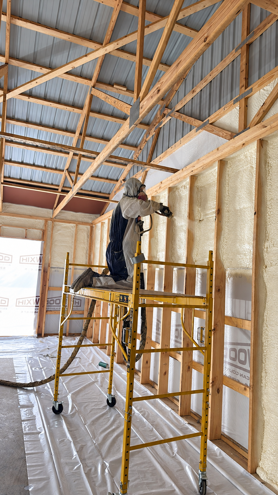 Technician applying spray foam insulation to a framed building from yellow scaffolding